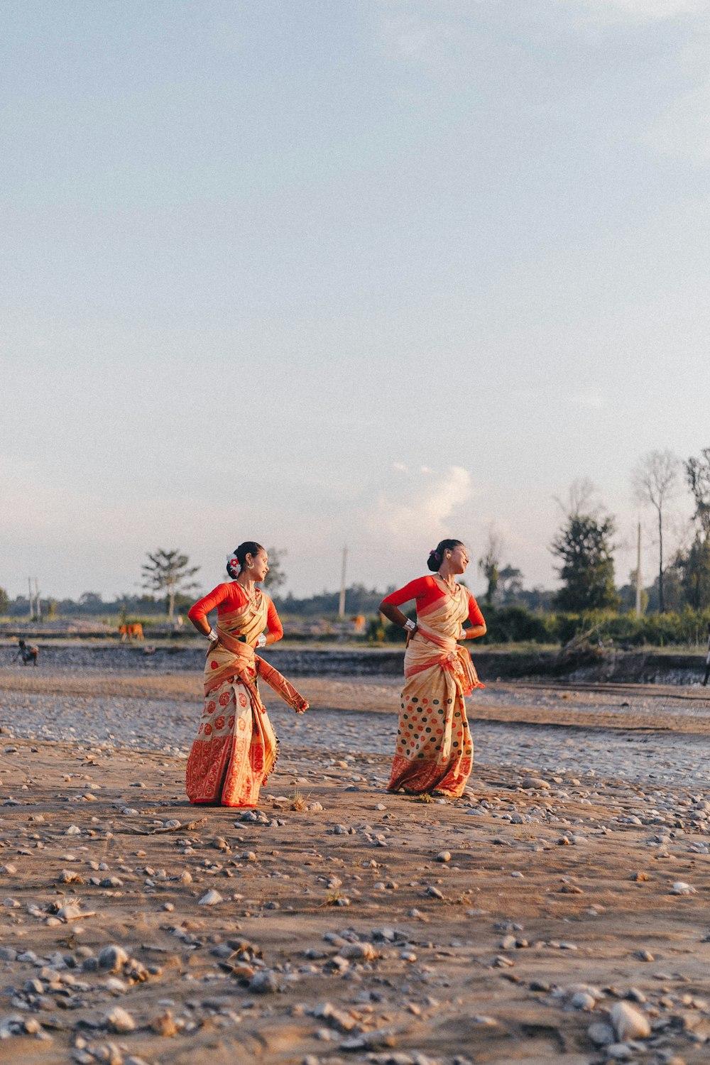 Two women in traditional Assamese dress walking on sand beside water