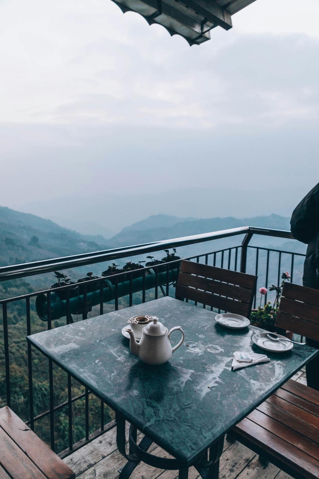 A teapot and cup on a stone table on a café balcony, looking out over misty blue hills