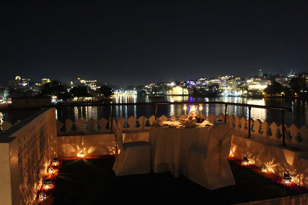 A candlelit dinner table on a palace rooftop at night, with the lights of Udaipur across the lake