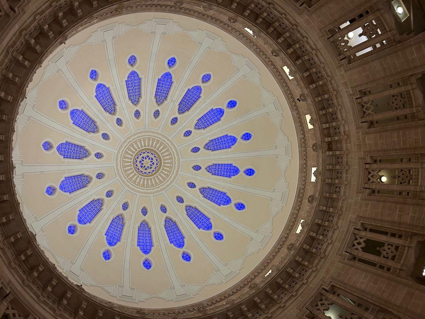 The inside of a sandstone dome, cream with a ring of blue glass panels, seen from below